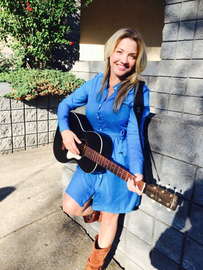 Annie Bonsignore in Nashville, standing in a blue dress and holding a black guitar